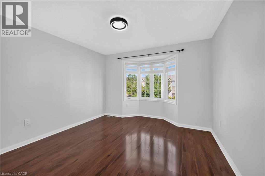 Bay window with multiple panes, wood-finish flooring, light gray wall paint, white trim, and a contemporary flush-mount ceiling light - 103 Emick Drive, Ancaster, ON