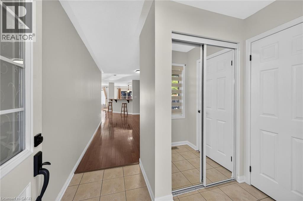 Entryway featuring ceramic tile flooring, a mirrored sliding closet door, and a paneled interior door, with wood-finish flooring extending into the background - 103 Emick Drive, Ancaster, ON
