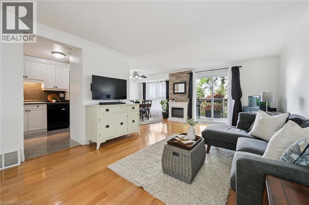 Hardwood-style flooring throughout, stone-clad fireplace, sliding glass doors to a private balcony, and an open concept kitchen with white cabinetry - 54 Green Valley Drive Unit# 13, Kitchener, ON