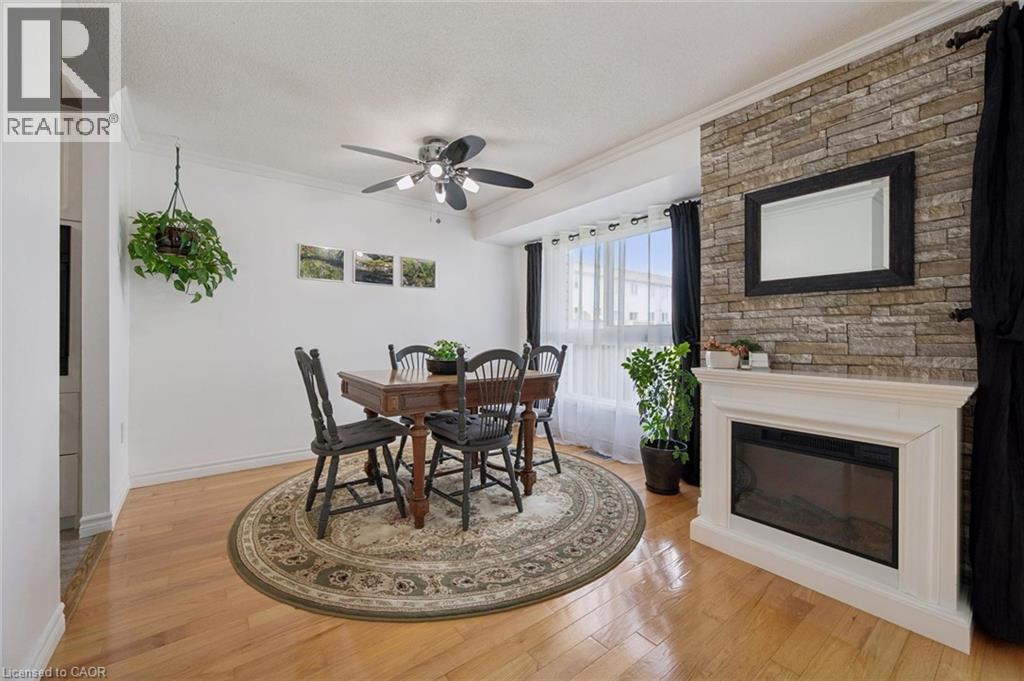 Hardwood flooring throughout, a ceiling fan with integrated lighting, a bay window with natural light, a stone-accented wall, and a built-in electric fireplace with a white mantel - 54 Green Valley Drive Unit# 13, Kitchener, ON