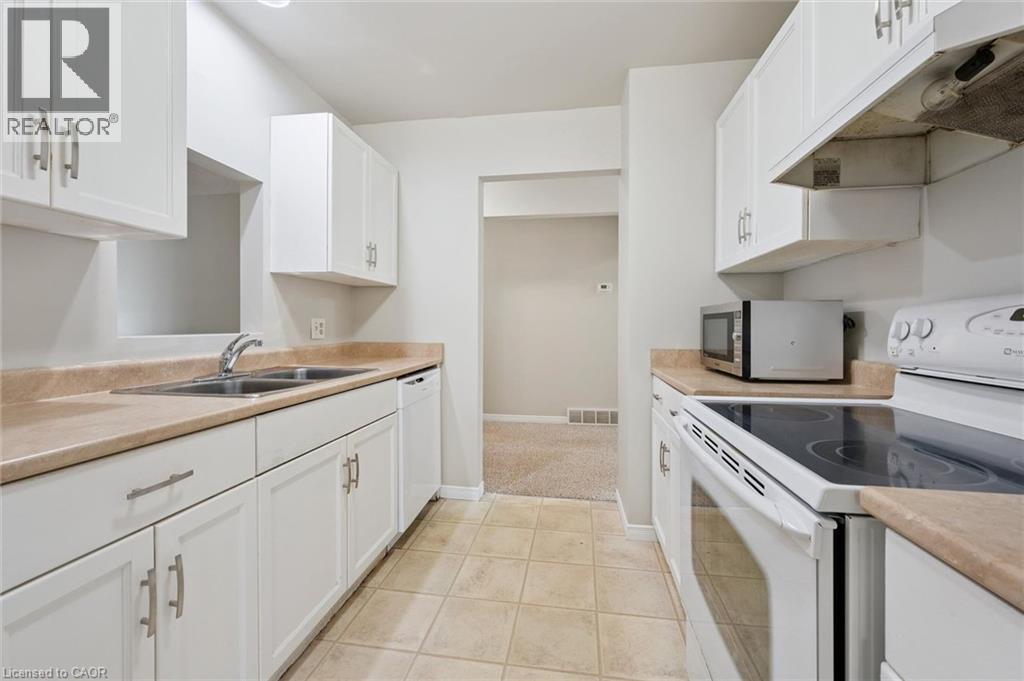 Kitchen featuring white cabinetry, light-toned countertops, a double basin sink, and tile flooring - 512 Thorndale Drive, Waterloo, ON
