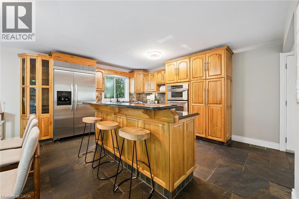 Stainless steel appliances, extensive wood cabinetry, an integrated kitchen island, dark stone-finish flooring, and built-in display shelving - 282 Concession Rd 2, Scotland, ON