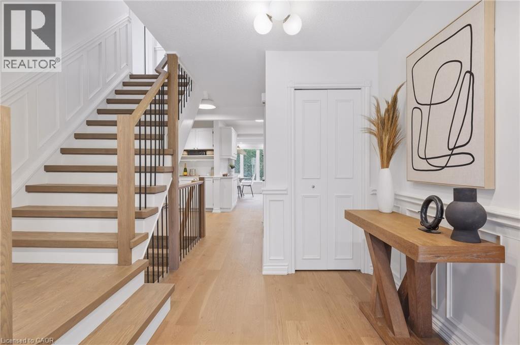 Light wood-finish flooring throughout, staircase with wood treads and metal balusters, wainscoting details, and bi-fold doors - 4159 Spruce Avenue, Burlington, ON