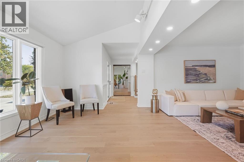 Bright open-concept living space showcasing wide-plank wood-finish flooring throughout, abundant natural light from large windows and glass doors, recessed ceiling lighting, and a neutral color palett - 4159 Spruce Avenue, Burlington, ON