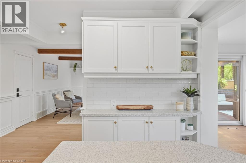 White shaker cabinetry with brass hardware, subway tile backsplash, wood-finish flooring, and exposed wood ceiling beams - 4159 Spruce Avenue, Burlington, ON