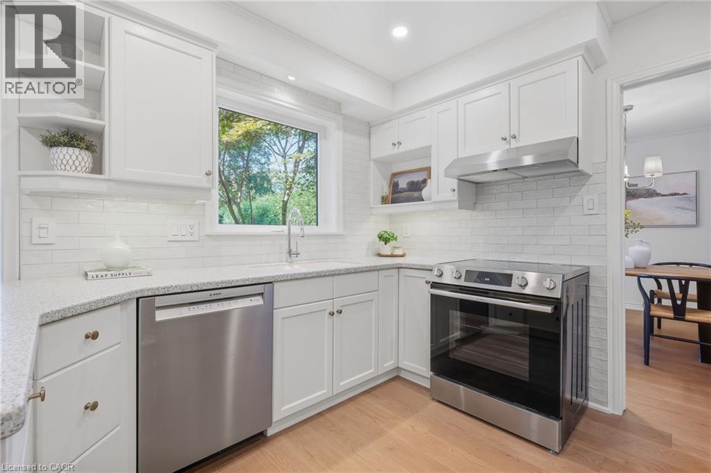White shaker cabinetry, stainless steel appliances, speckled countertops, white subway tile backsplash, and light wood-finish flooring - 4159 Spruce Avenue, Burlington, ON