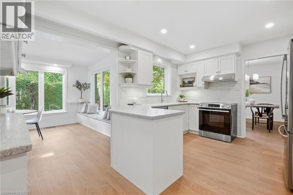 White shaker cabinetry paired with stainless steel appliances, light wood-finish flooring, and a subway tile backsplash - 4159 Spruce Avenue, Burlington, ON