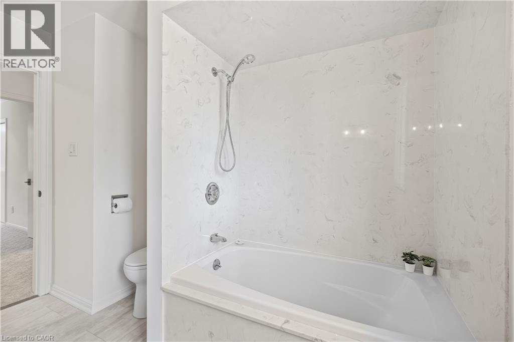 Integrated tub and shower combination with white surround, chrome fixtures, and a handheld showerhead - 4159 Spruce Avenue, Burlington, ON