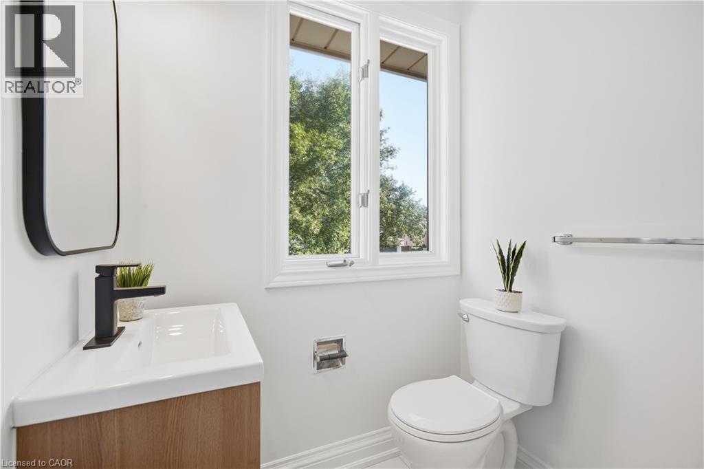 Wood-finish vanity with an integrated white sink, matte black faucet, and a rectangular black-framed mirror - 4159 Spruce Avenue, Burlington, ON
