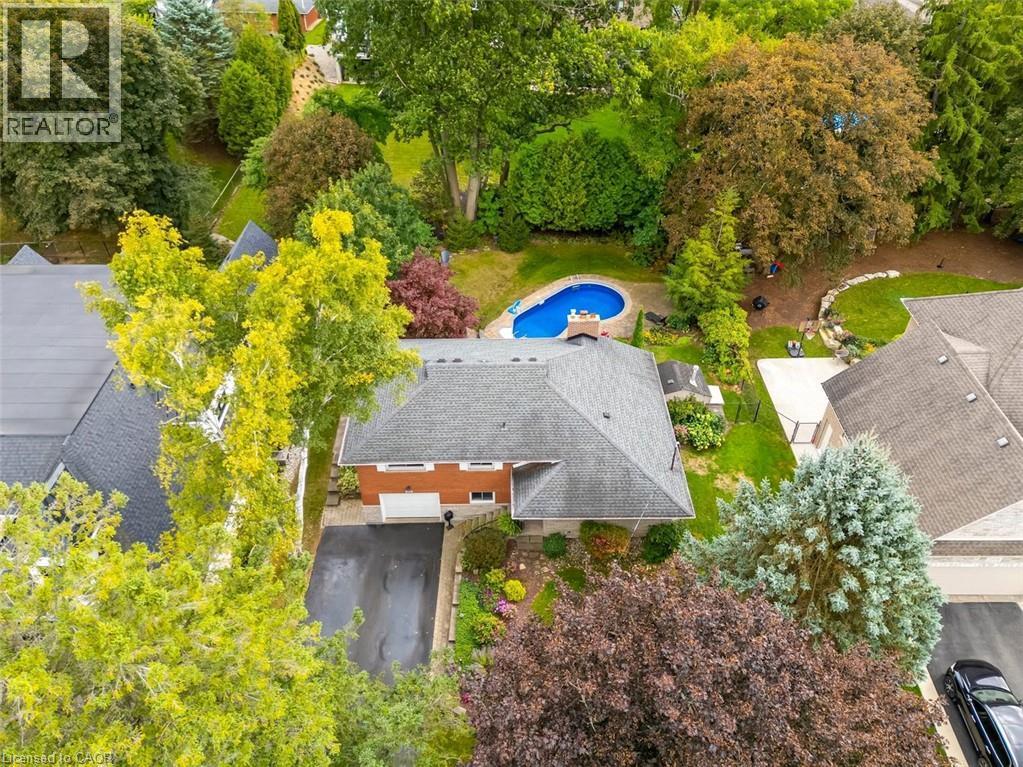 Aerial view of Kidney-shaped swimming pool with stone surround, integrated hot tub, extensive paving stone patio, and mature trees - 200 Woodview Crescent, Ancaster, ON