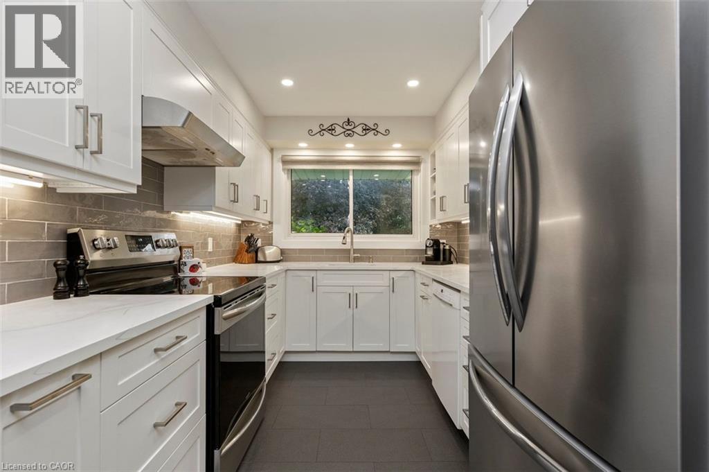 White cabinetry, stainless steel appliances, quartz counters and subway tile. View to front yard - 200 Woodview Crescent, Ancaster, ON