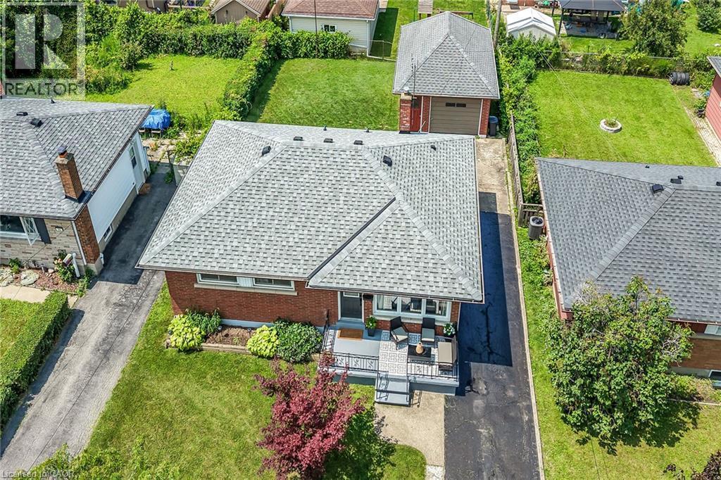 Brick residence with a light gray shingle roof, featuring a front porch with dark railing, landscaped front yard, and an asphalt driveway leading to a detached garage - 13 Allanburg Road S, St. Catharines, ON