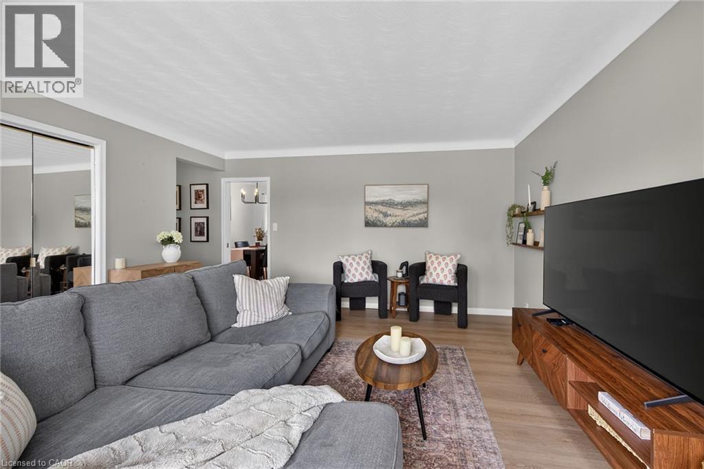 Spacious living area featuring light gray wall tones, crown molding, wood-finish flooring, and a mirrored closet - 13 Allanburg Road S, St. Catharines, ON