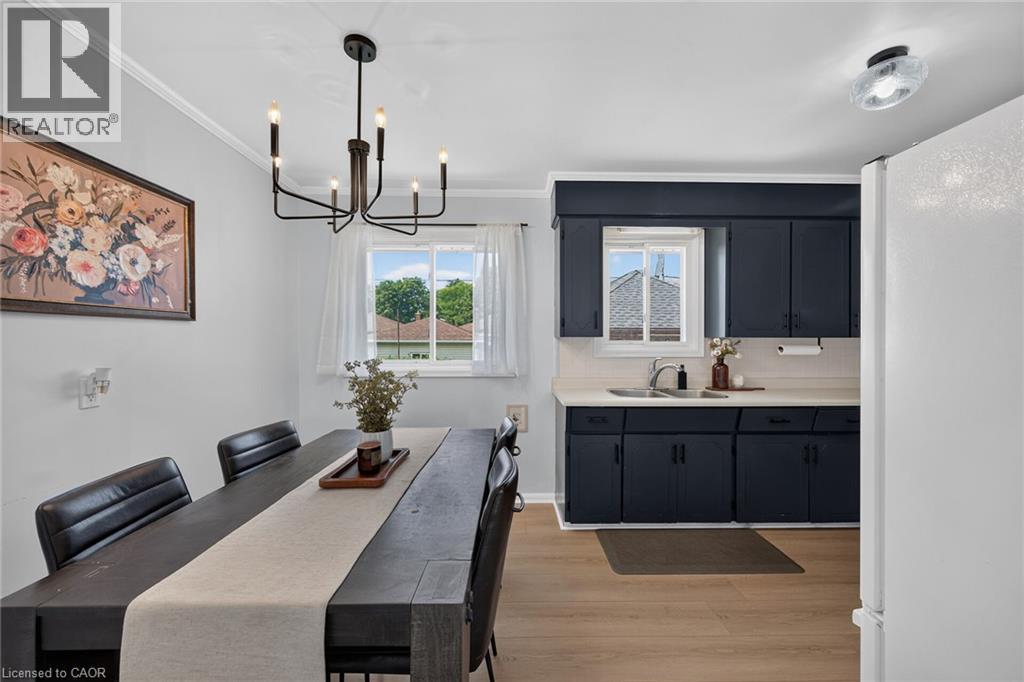 Modern dining and kitchen area featuring a wood-finish floor, sleek black cabinetry with ample storage, stainless steel appliances, and a spacious dining table with seating for multiple guests - 13 Allanburg Road S, St. Catharines, ON