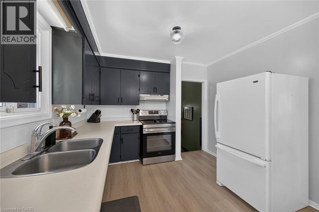 Kitchen featuring black cabinetry, stainless steel range, double basin sink, light-toned countertops, and wood-finish flooring - 13 Allanburg Road S, St. Catharines, ON