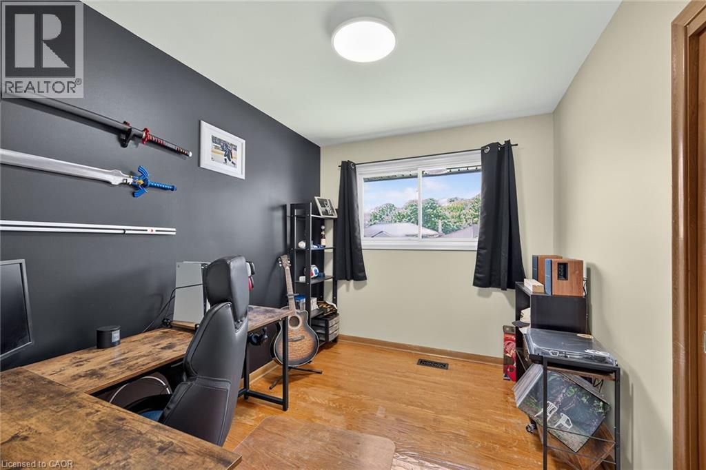 Versatile bonus room featuring hardwood flooring, a dark accent wall with mounted shelving and rod systems, recessed ceiling lighting, and a large window with black-framed glass - 13 Allanburg Road S, St. Catharines, ON