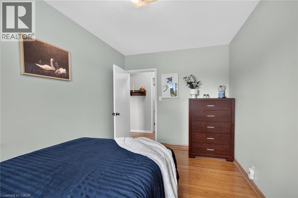 Bedroom with light gray walls, wood-finish flooring, a white ceiling, and an open doorway revealing a closet with a built-in shelf - 13 Allanburg Road S, St. Catharines, ON
