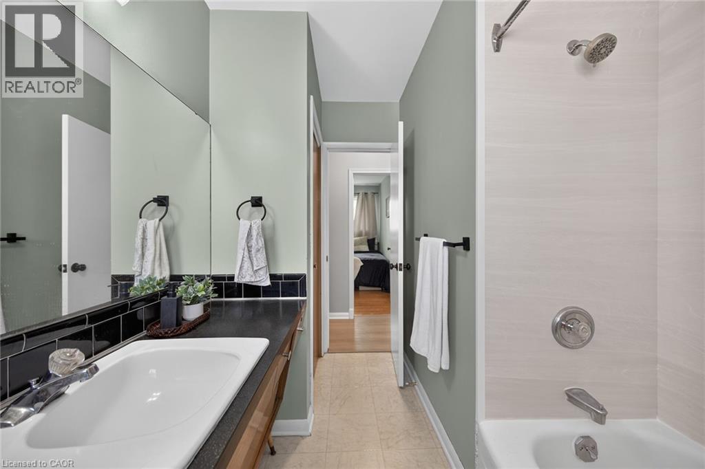 Bathroom featuring a white porcelain sink set into a dark countertop, black subway tile backsplash, and an integrated mirror - 13 Allanburg Road S, St. Catharines, ON