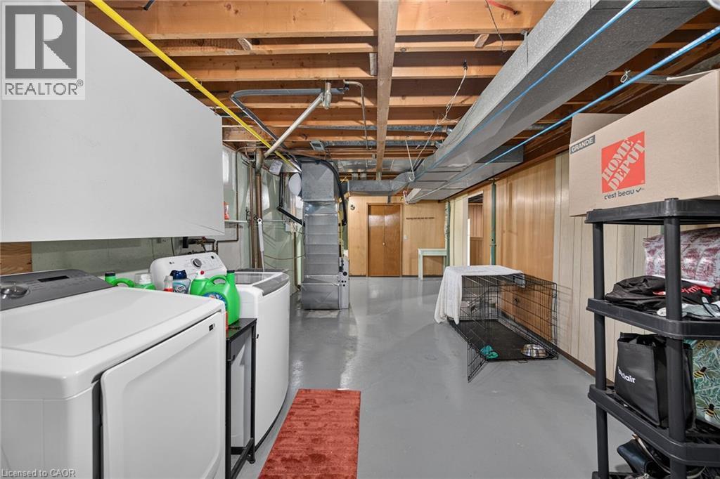 Basement utility area featuring a washer and dryer, painted concrete flooring, wood paneling, and exposed ceiling joists - 13 Allanburg Road S, St. Catharines, ON