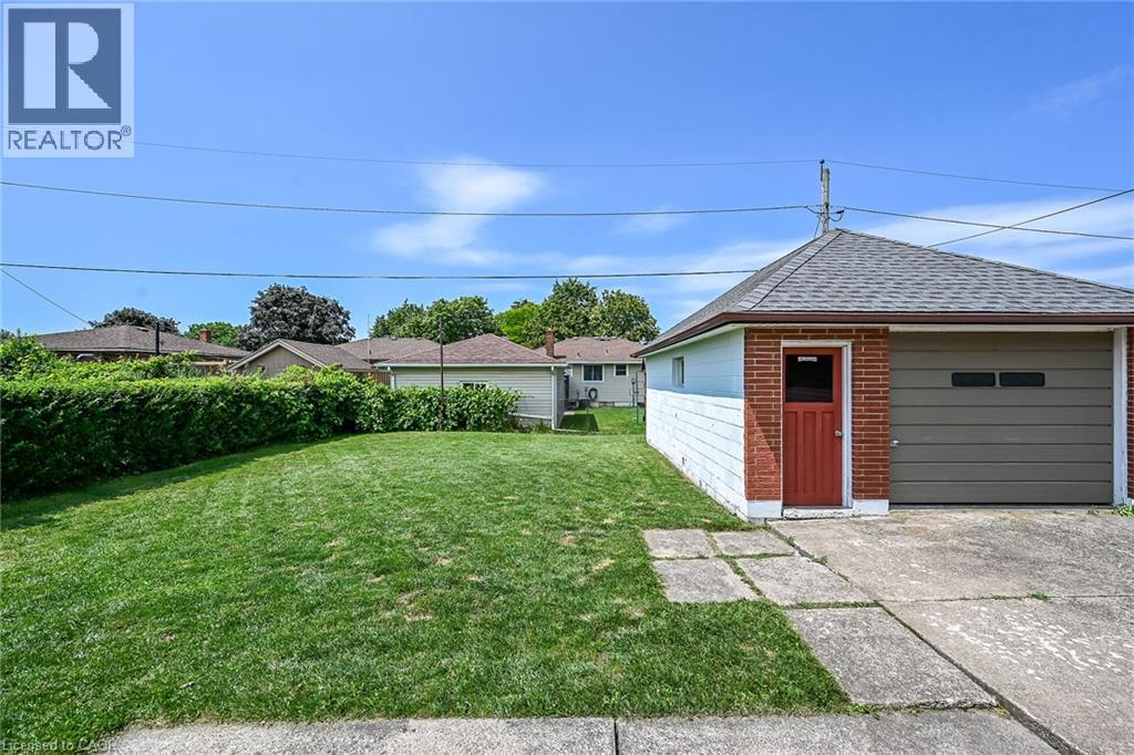 Detached garage featuring brick and siding exterior, a red entry door, a gray garage door, and shingle roofing - 13 Allanburg Road S, St. Catharines, ON