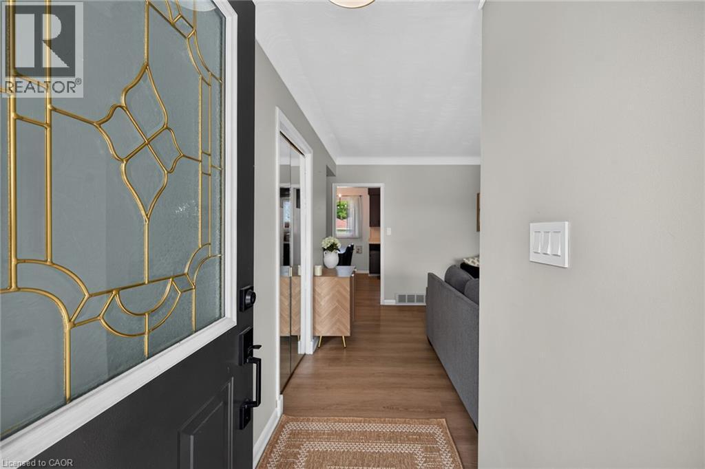 Entryway featuring a dark paneled door with decorative leaded glass, wood-finish flooring, light gray wall paint, and white trim - 13 Allanburg Road S, St. Catharines, ON