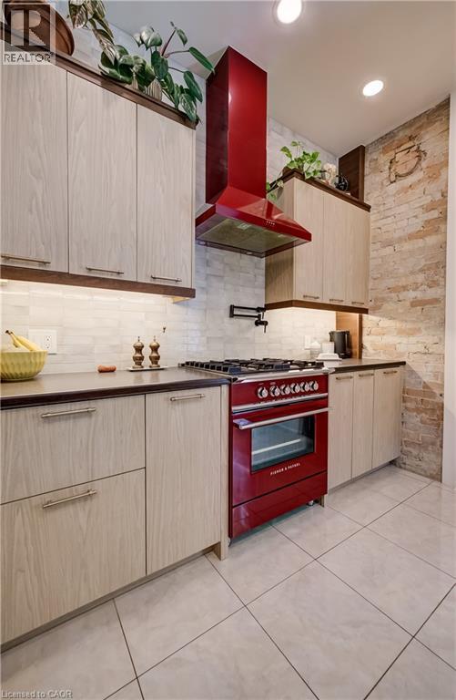 Kitchen featuring a red range with matching hood, light wood-finish cabinetry, dark countertops, a white tile backsplash, and light tile flooring - 59 Allen Street W, Waterloo, ON