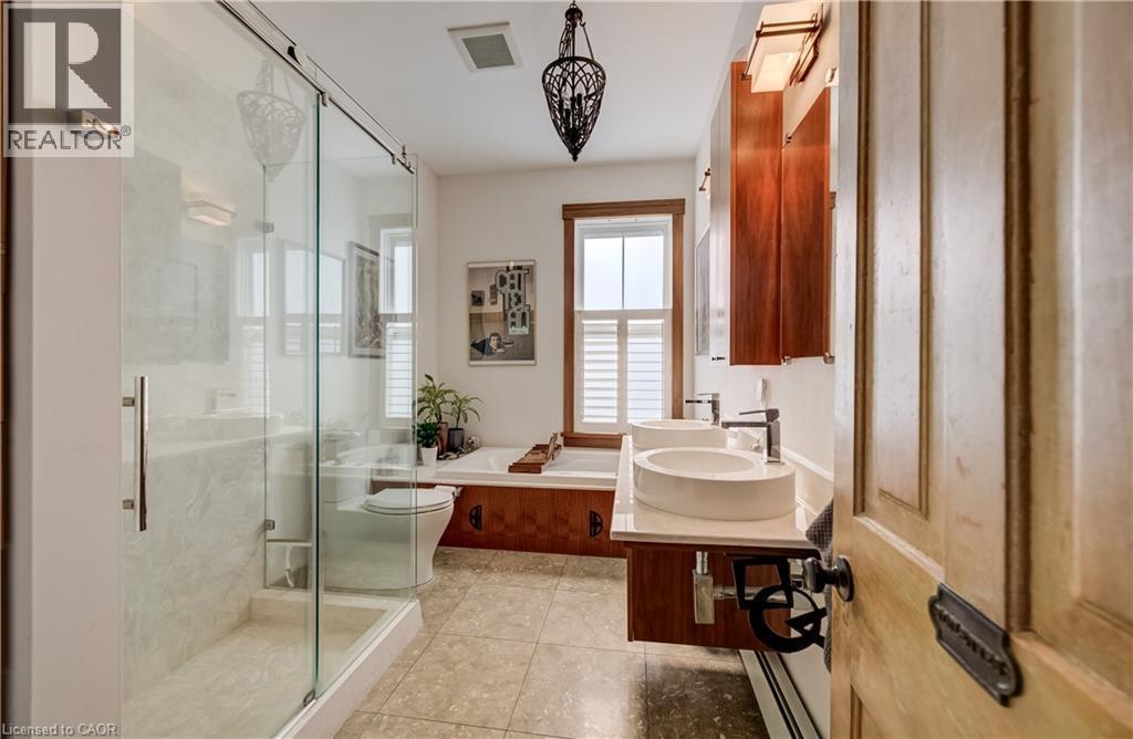Glass-enclosed shower with tiled walls and floor, dual vessel sinks with wall-mounted faucets, built-in soaking tub with wood surround, and tiled flooring - 59 Allen Street W, Waterloo, ON