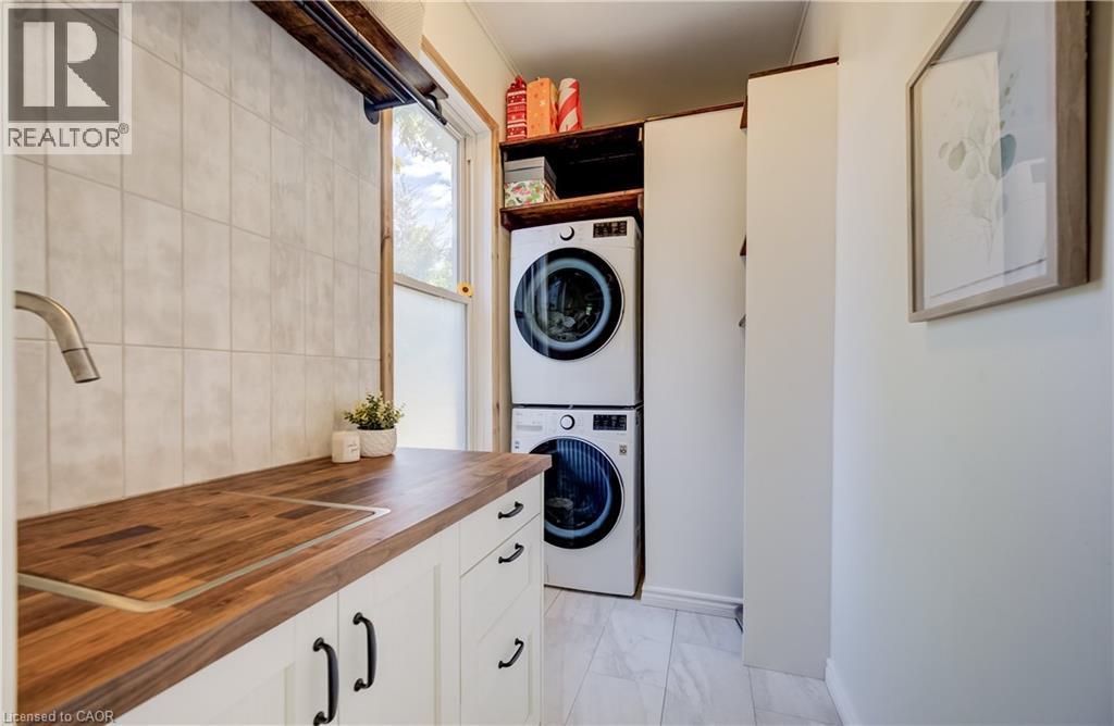 Built-in cabinetry with wood-finish countertop, undermount sink with gooseneck faucet, full-height tile backsplash, and stacked laundry appliances - 59 Allen Street W, Waterloo, ON