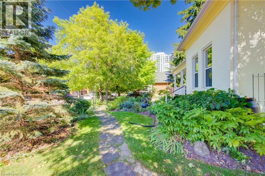 Stucco exterior with multiple windows, complemented by a stone-paver pathway, mature trees, and established landscaping - 59 Allen Street W, Waterloo, ON