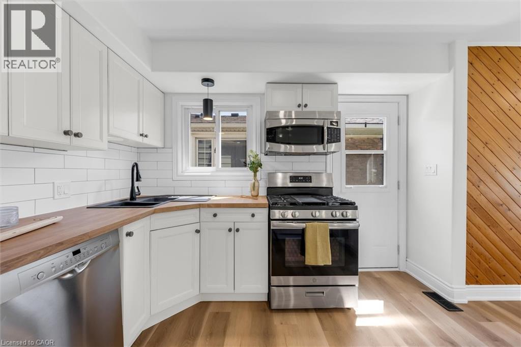 Kitchen featuring wood-finish flooring, white cabinetry, wood countertops, a black sink, and stainless steel appliances - 49 Grove Avenue, St. Catharines, ON