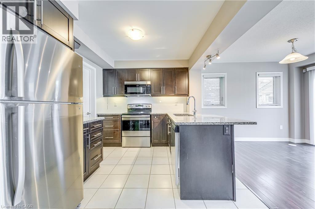 Kitchen featuring stainless steel appliances, dark wood-finish cabinetry, granite-finish countertops, and white tile flooring - 212 Ellen Davidson Drive, Oakville, ON
