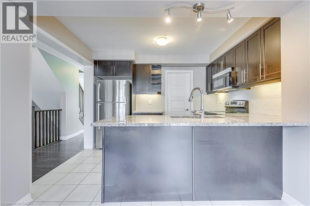 Kitchen featuring a stainless steel refrigerator, dark wood-finish cabinetry, a large kitchen island with a stone countertop, and integrated stainless steel appliances - 212 Ellen Davidson Drive, Oakville, ON