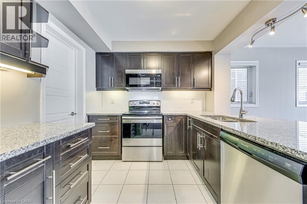Kitchen featuring dark wood-finish cabinetry, light-toned granite countertops, and stainless steel appliances - 212 Ellen Davidson Drive, Oakville, ON