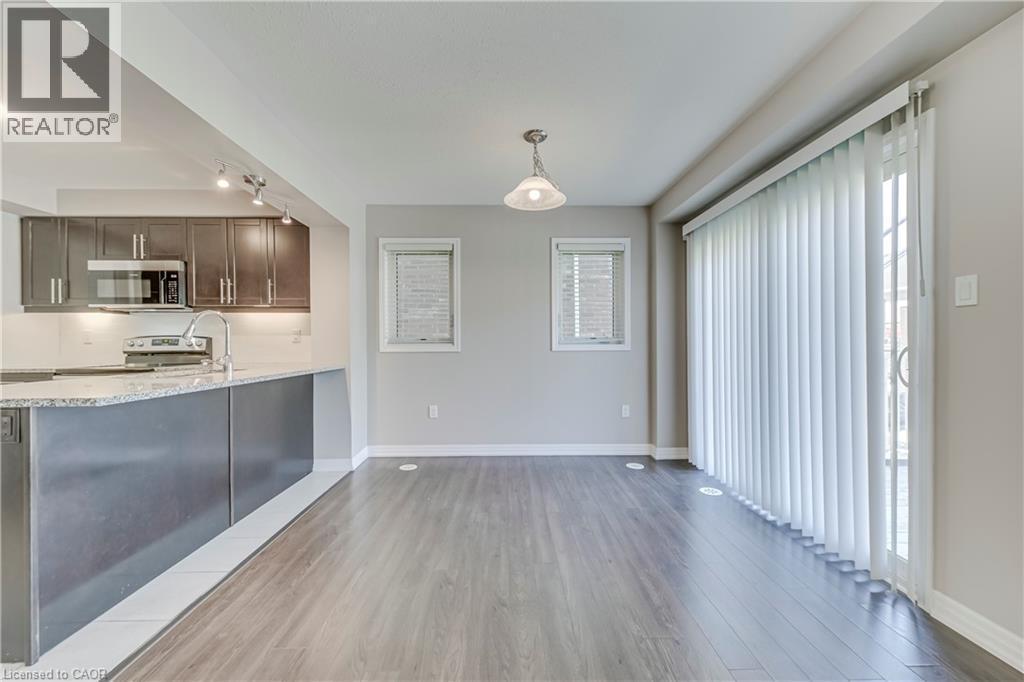 Open-concept layout featuring wood-finish flooring, a kitchen with dark cabinetry and light-toned countertops, and a sliding glass door - 212 Ellen Davidson Drive, Oakville, ON