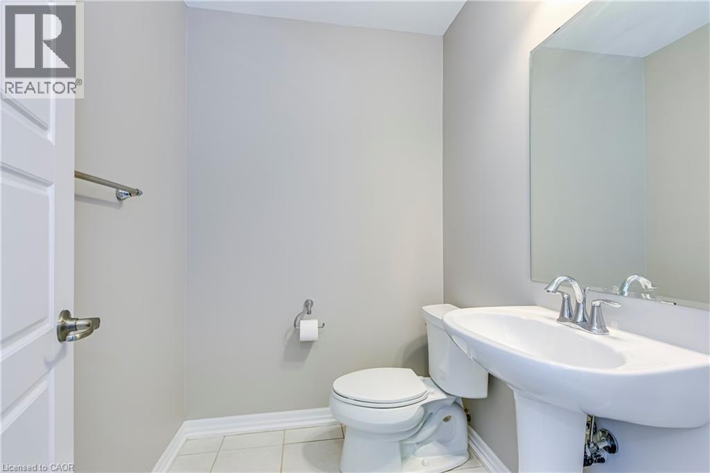Pedestal sink with chrome fixtures, wall-mounted mirror, white toilet, and light-colored tile flooring - 212 Ellen Davidson Drive, Oakville, ON