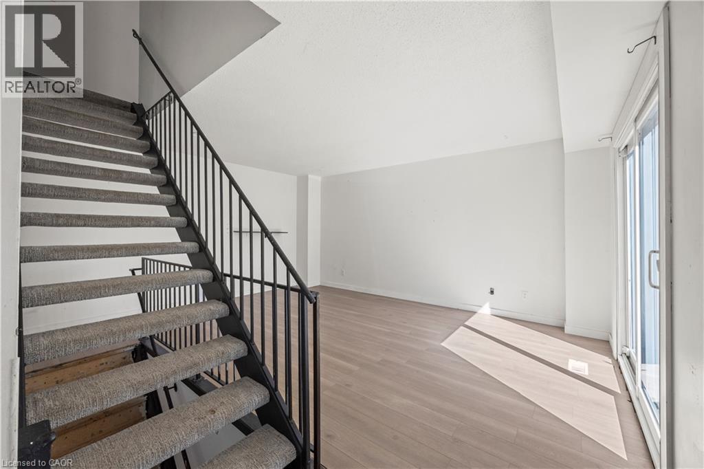 Staircase with carpeted treads and black metal railing, wood-finish flooring, and sliding glass door - 70 Fiddlers Green Road Unit# 74, London, ON