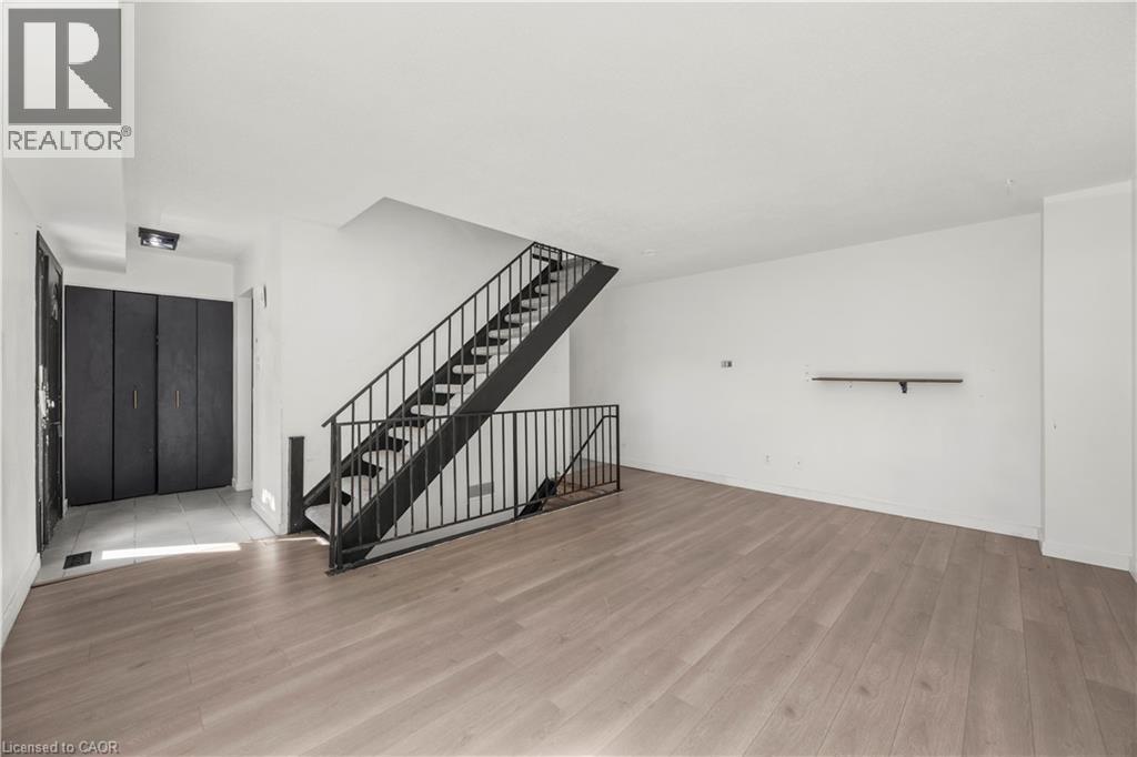 Expansive room with wood-finish flooring, white walls, and a black metal staircase - 70 Fiddlers Green Road Unit# 74, London, ON