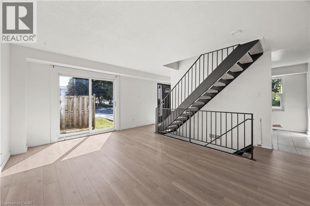 Spacious living area featuring wood-finish flooring, a contemporary staircase with metal railings, a sliding glass door, and white painted walls - 70 Fiddlers Green Road Unit# 74, London, ON