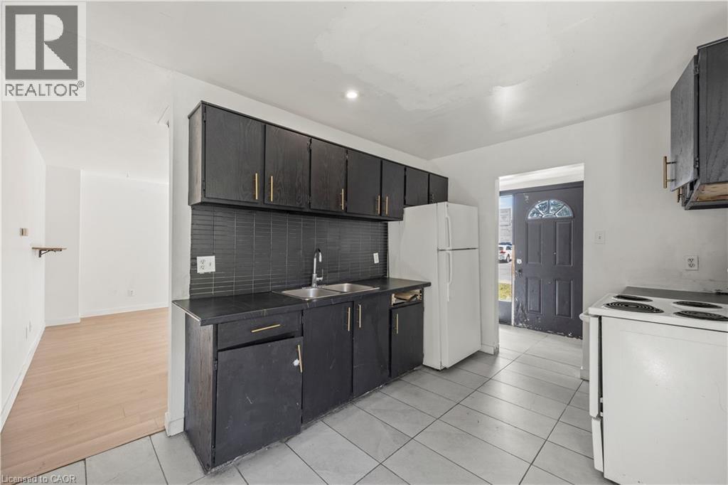 Kitchen featuring dark cabinetry, a coordinating dark backsplash, a stainless steel sink, and tile flooring - 70 Fiddlers Green Road Unit# 74, London, ON