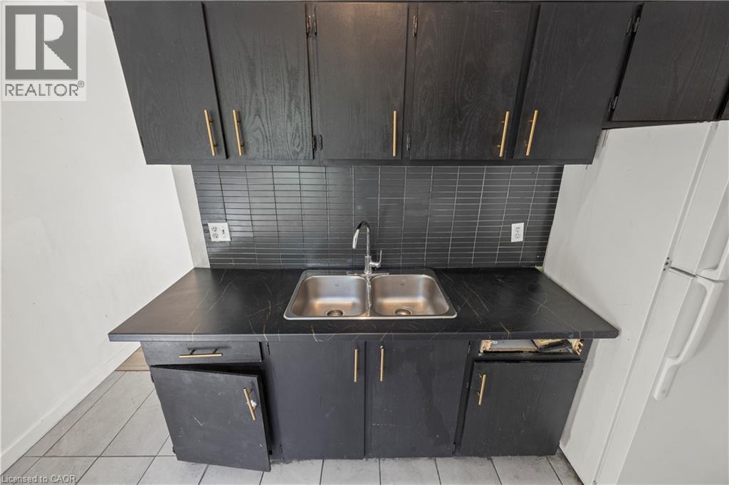 Black cabinetry with gold-finish hardware, black subway tile backsplash, and a double basin stainless steel sink - 70 Fiddlers Green Road Unit# 74, London, ON