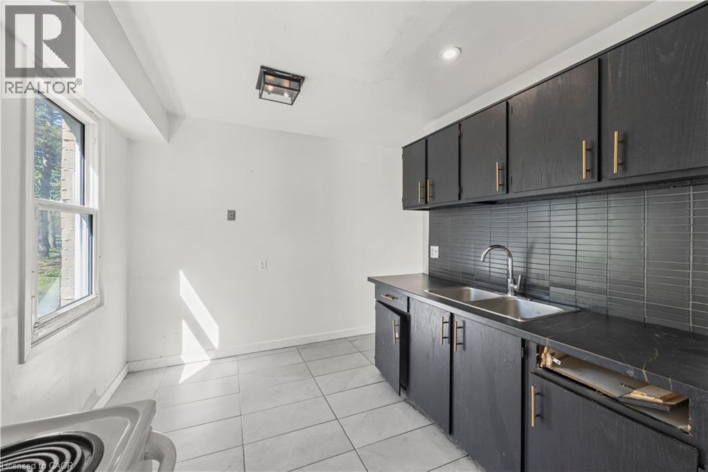 Black cabinetry with gold-tone hardware, dark countertop, dual basin stainless steel sink, subway tile backsplash, and light-toned tile flooring - 70 Fiddlers Green Road Unit# 74, London, ON