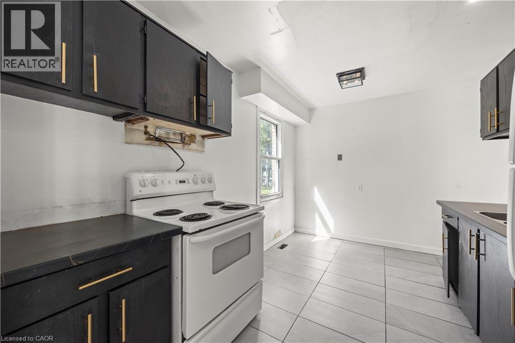 Kitchen featuring black cabinetry with gold-toned hardware, white electric range, and tiled flooring - 70 Fiddlers Green Road Unit# 74, London, ON