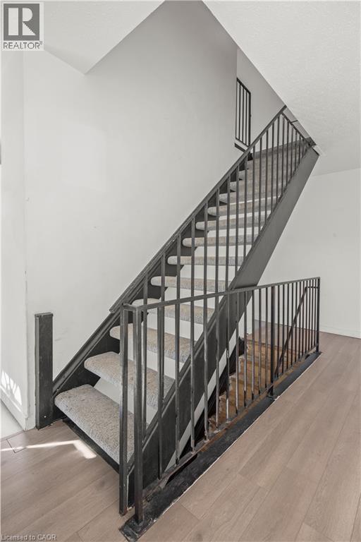 Staircase featuring wood-finish flooring, metal railings, and carpeted treads - 70 Fiddlers Green Road Unit# 74, London, ON