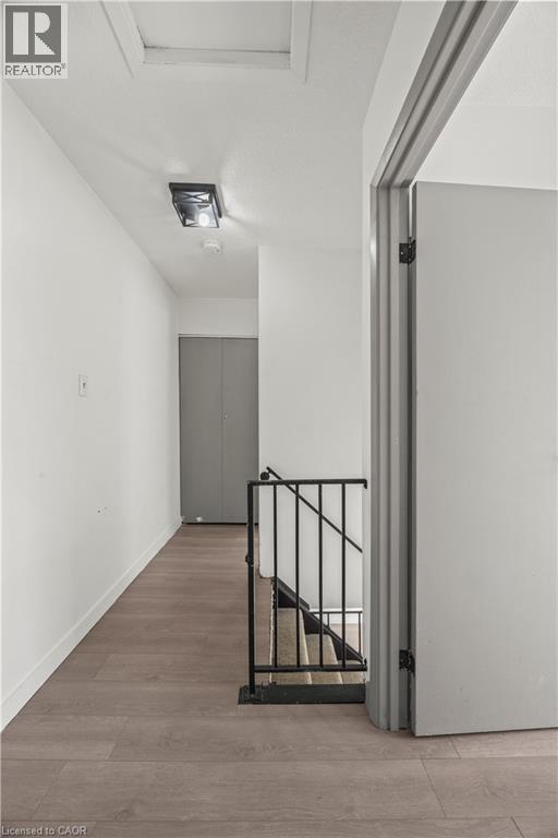 Hallway with wood-finish flooring, white walls, and a black wrought iron stair railing - 70 Fiddlers Green Road Unit# 74, London, ON
