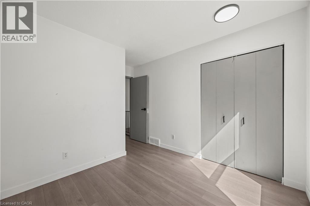 Wood-finish flooring, white walls, bi-fold closet doors, contemporary flush mount ceiling light fixture, and a modern interior door - 70 Fiddlers Green Road Unit# 74, London, ON