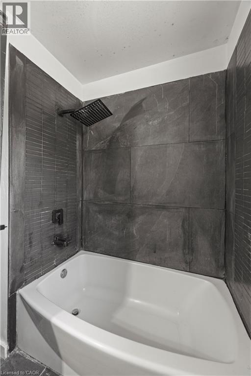 White drop-in bathtub with dark stone-finish wall tile and a square rain showerhead - 70 Fiddlers Green Road Unit# 74, London, ON