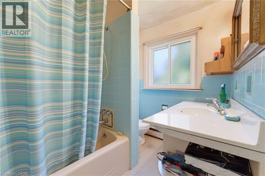 Enclosed bath with light blue wall tiling, built-in tub, and wall-mounted sink with integrated countertop - 940 Harvey Place, Halton, ON
