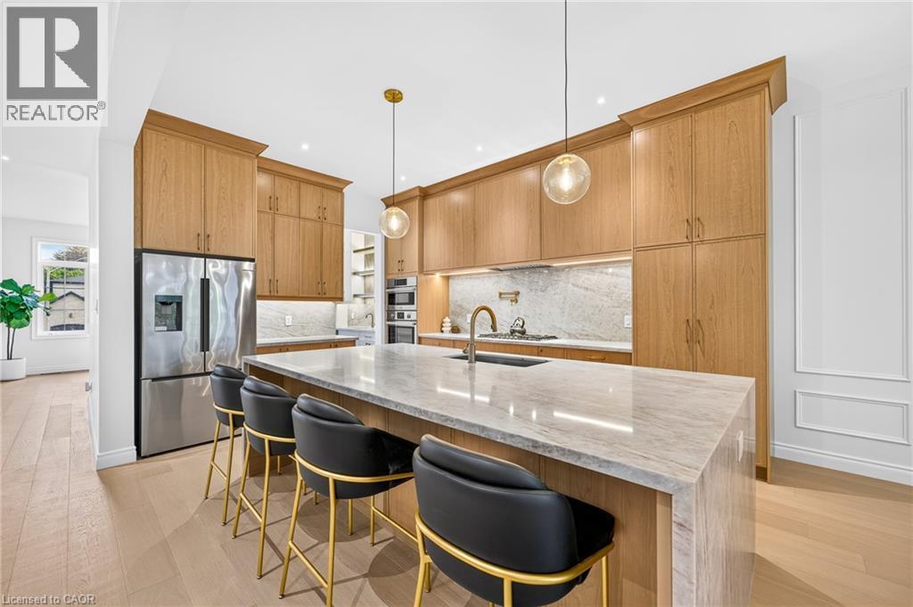 Gourmet kitchen featuring custom wood cabinetry, stainless steel appliances, a large center island with stone countertop, and pendant lighting - 67 Cielo Court, Hamilton, ON