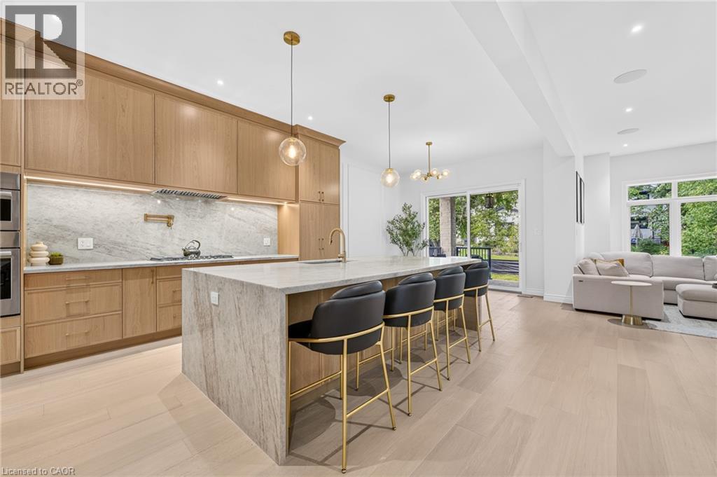 Light wood-finish flooring, full-height cabinetry, kitchen island with seating, stainless steel appliances, and a sliding glass door - 67 Cielo Court, Hamilton, ON