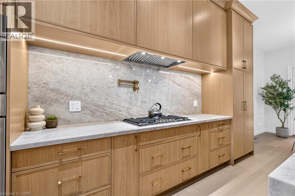 Custom light wood-finish cabinetry, solid surface countertops, patterned backsplash, built-in gas range, and a pot filler - 67 Cielo Court, Hamilton, ON